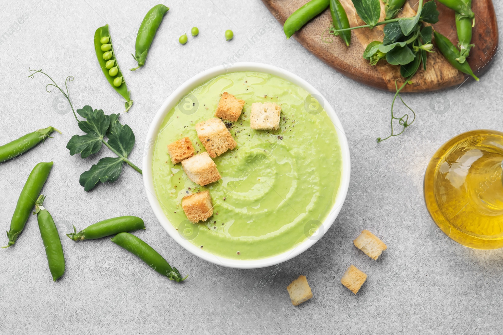 Photo of Tasty pea cream soup with croutons served on grey table, flat lay