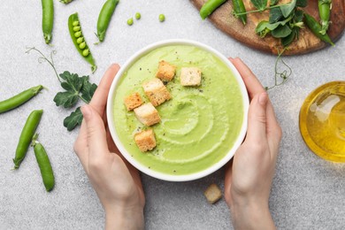 Photo of Woman having tasty pea cream soup with croutons at grey table, top view