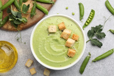 Photo of Tasty pea cream soup with croutons served on grey table, flat lay