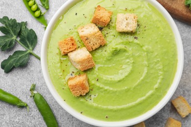 Photo of Tasty pea cream soup with croutons served on grey table, flat lay