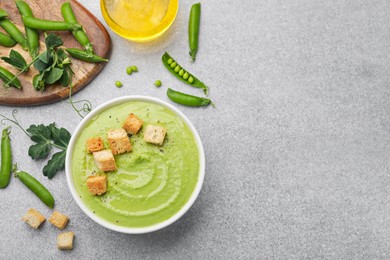 Photo of Tasty pea cream soup with croutons served on grey table, flat lay. Space for text