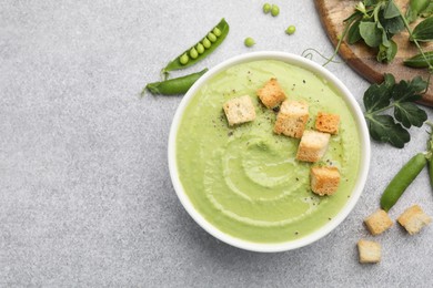 Photo of Tasty pea cream soup with croutons served on grey table, flat lay