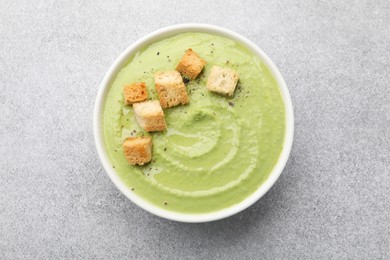 Photo of Tasty pea cream soup with croutons on grey table, top view