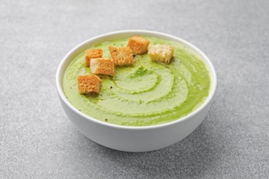 Photo of Tasty pea cream soup with croutons on grey table, closeup