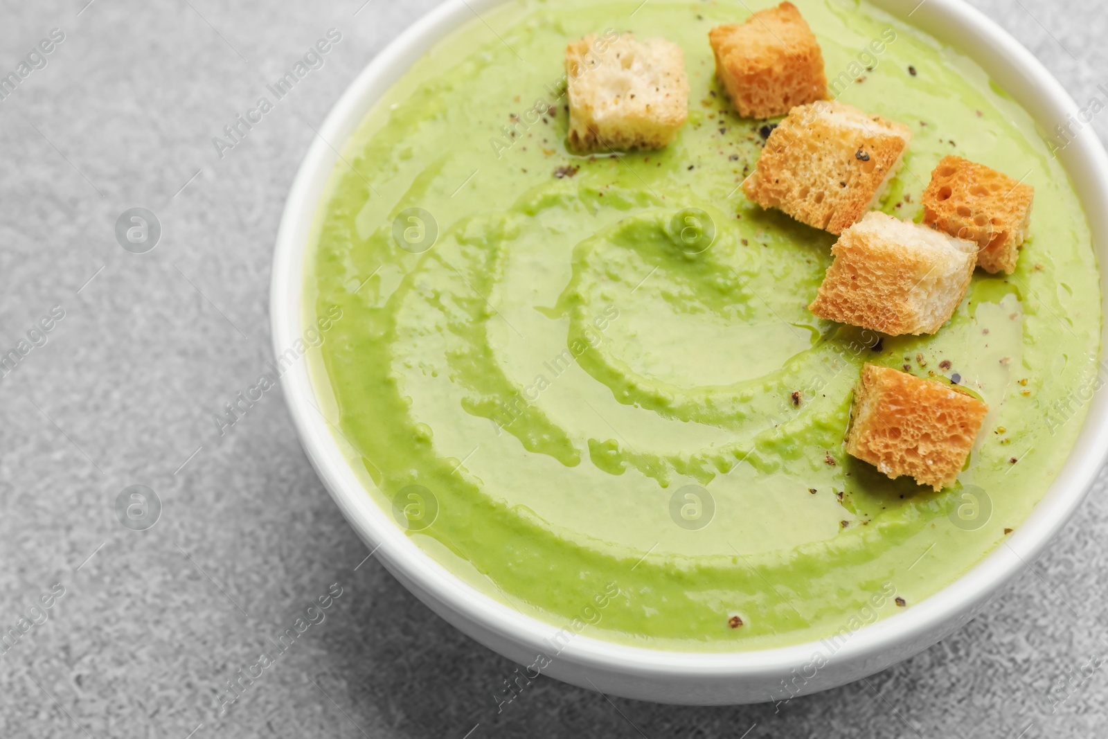 Tasty pea cream soup with croutons on grey table, closeup Photo of Tasty pea cream soup with croutons on grey table, closeup