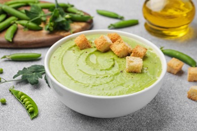 Photo of Tasty pea cream soup with croutons served on grey table, closeup
