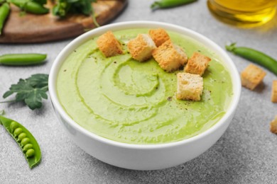Photo of Tasty pea cream soup with croutons served on grey table, closeup