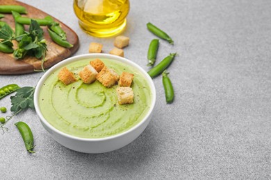 Photo of Tasty pea cream soup with croutons served on grey table. Space for text