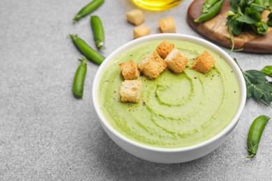 Photo of Tasty pea cream soup with croutons served on grey table, closeup