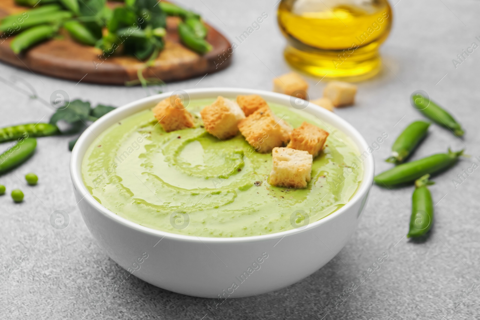 Photo of Tasty pea cream soup with croutons served on grey table, closeup