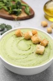 Photo of Tasty pea cream soup with croutons served on grey table, closeup