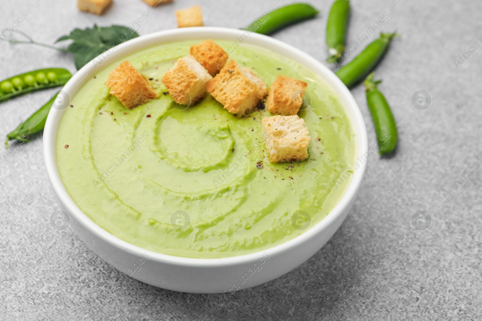 Photo of Tasty pea cream soup with croutons served on grey table, closeup