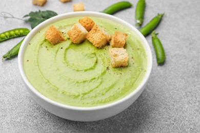 Photo of Tasty pea cream soup with croutons served on grey table, closeup