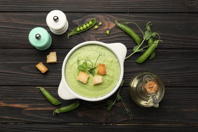 Photo of Tasty pea cream soup with croutons served on dark wooden table, flat lay