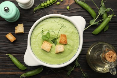 Photo of Tasty pea cream soup with croutons served on dark wooden table, flat lay