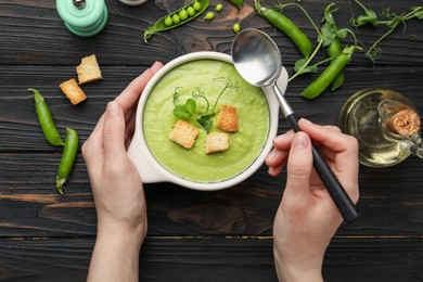 Photo of Woman eating tasty pea cream soup at wooden table, top view