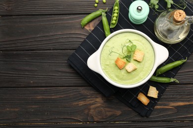 Photo of Tasty pea cream soup with croutons served on dark wooden table, flat lay. Space for text