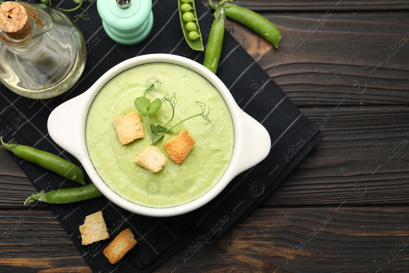 Photo of Tasty pea cream soup with croutons served on dark wooden table, flat lay