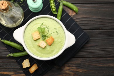 Photo of Tasty pea cream soup with croutons served on dark wooden table, flat lay