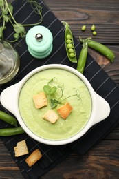 Photo of Tasty pea cream soup with croutons served on dark wooden table, flat lay