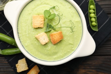 Photo of Tasty pea cream soup with croutons served on dark wooden table, flat lay