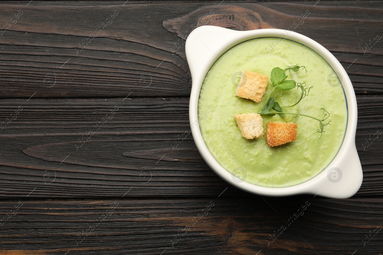 Tasty pea cream soup with croutons and microgreens on dark wooden table, top view. Space for text Photo of Tasty pea cream soup with croutons and microgreens on dark wooden table, top view. Space for text