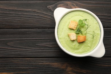 Photo of Tasty pea cream soup with croutons and microgreens on dark wooden table, top view. Space for text