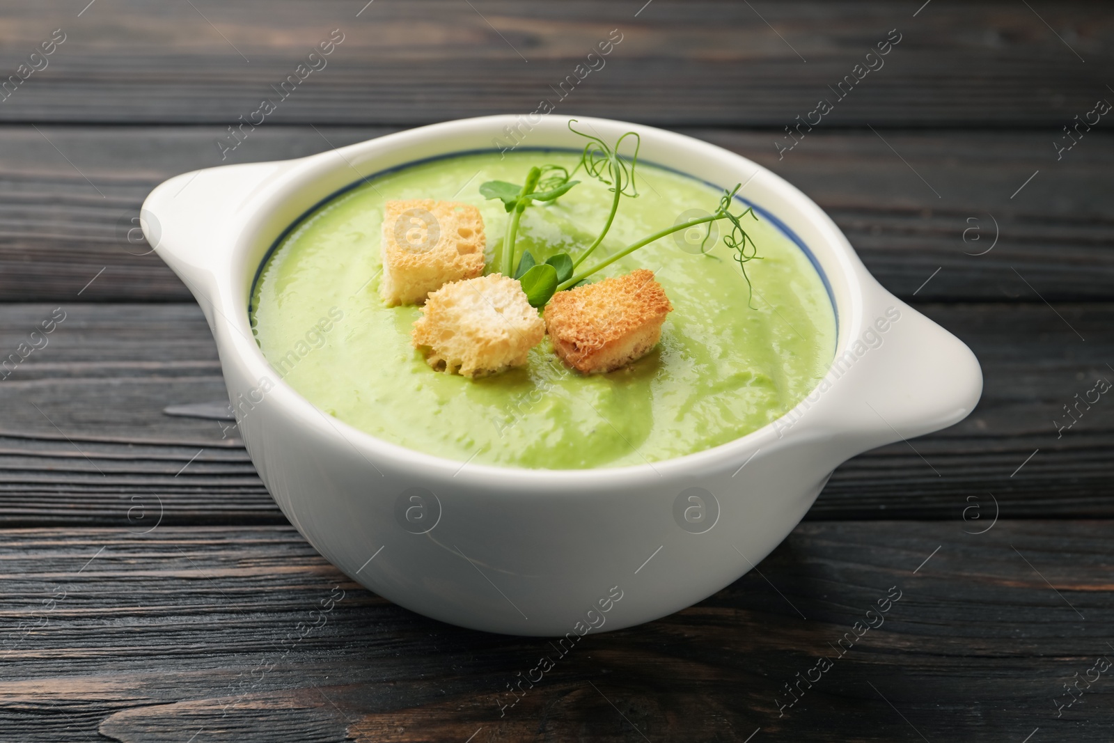 Photo of Tasty pea cream soup with croutons and microgreens on dark wooden table, closeup