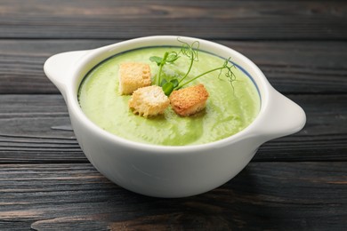 Photo of Tasty pea cream soup with croutons and microgreens on dark wooden table, closeup
