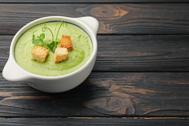 Photo of Tasty pea cream soup with croutons and microgreens on dark wooden table. Space for text