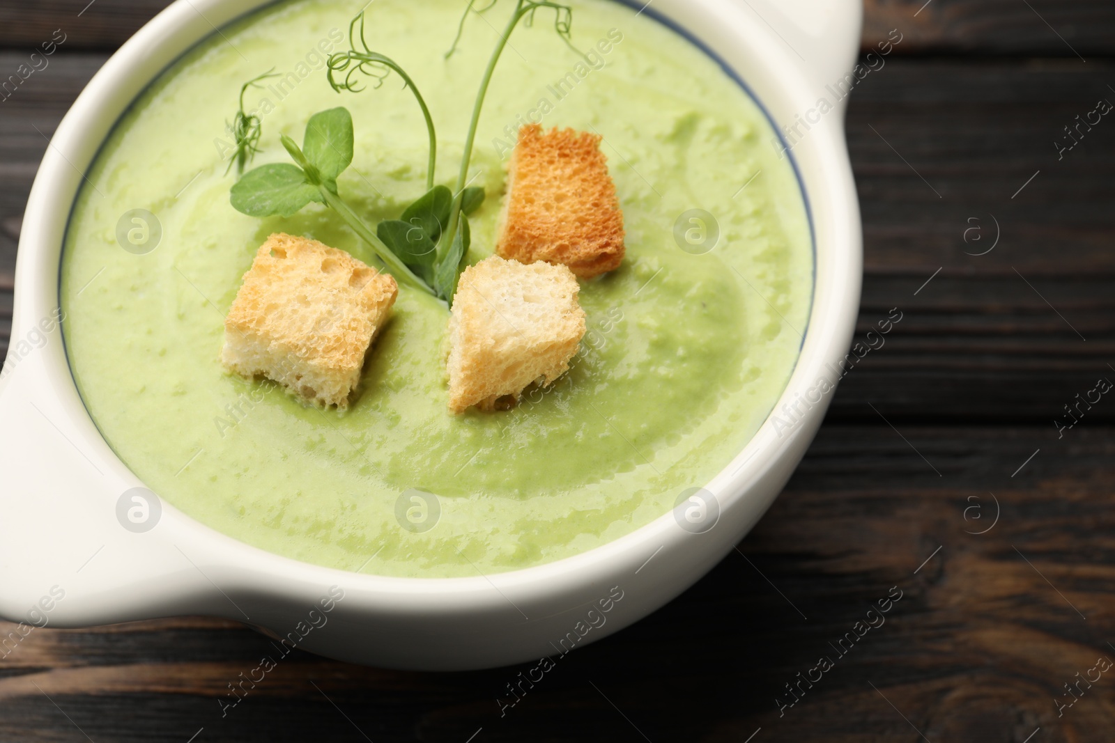 Tasty pea cream soup with croutons and microgreens on dark wooden table, closeup Photo of Tasty pea cream soup with croutons and microgreens on dark wooden table, closeup