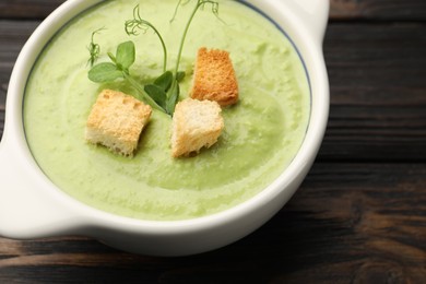 Photo of Tasty pea cream soup with croutons and microgreens on dark wooden table, closeup