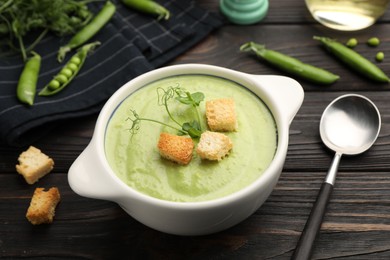 Photo of Tasty pea cream soup with croutons served on dark wooden table, closeup