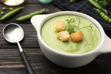 Photo of Tasty pea cream soup with croutons served on dark wooden table, closeup