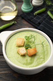 Photo of Tasty pea cream soup with croutons served on dark wooden table, closeup