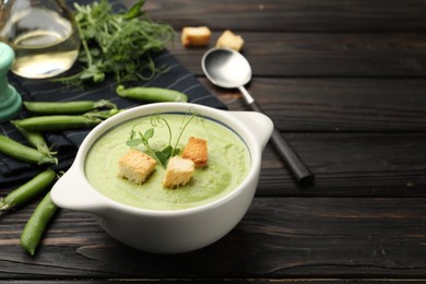 Photo of Tasty pea cream soup with croutons served on dark wooden table. Space for text