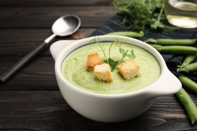 Photo of Tasty pea cream soup with croutons served on dark wooden table, closeup