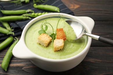 Photo of Tasty pea cream soup with croutons served on dark wooden table, closeup