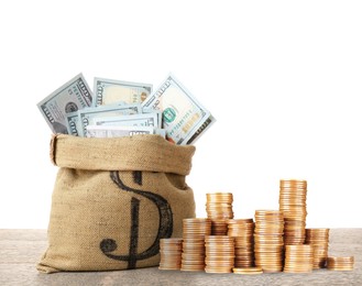 Image of Wealth. Burlap bag full of dollar bills and stacked coins on wooden table against white background