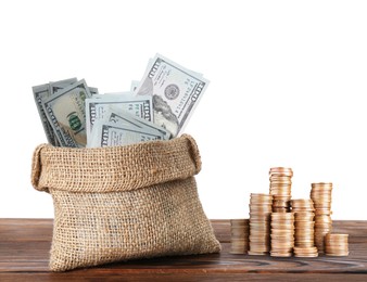 Image of Wealth. Burlap bag full of dollar bills and stacked coins on wooden table against white background
