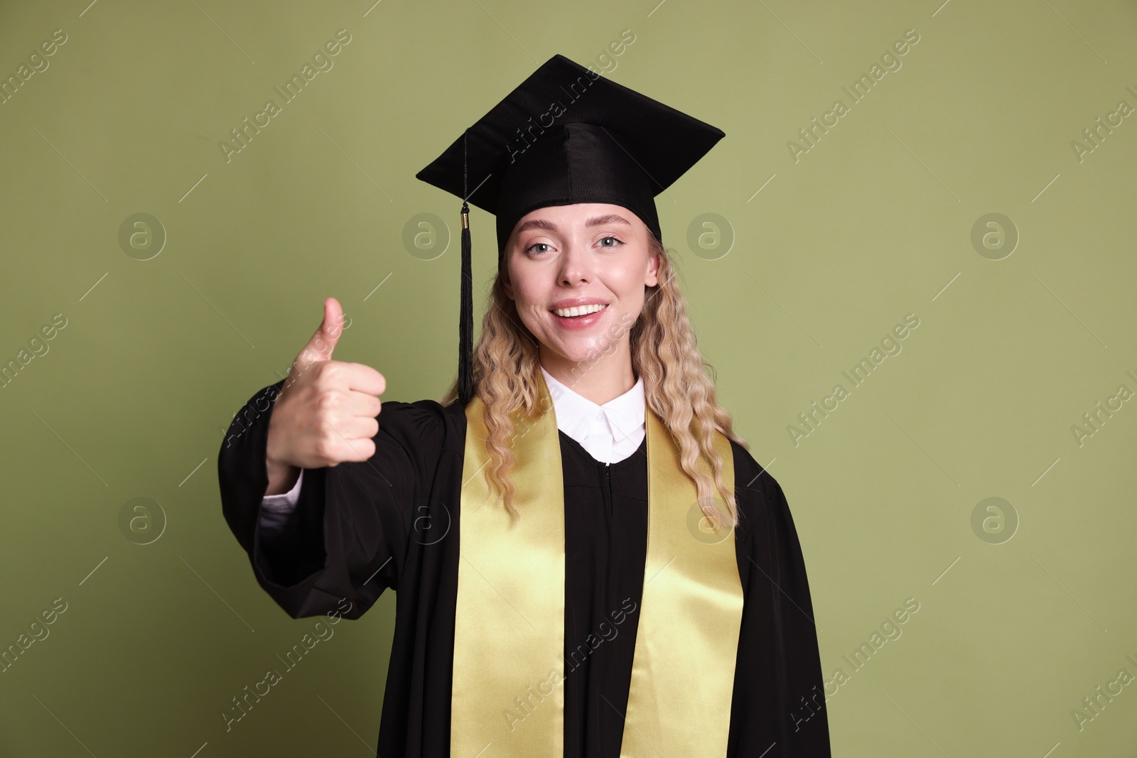 Happy student showing thumbs up after graduation on green background Photo of Happy student showing thumbs up after graduation on green background