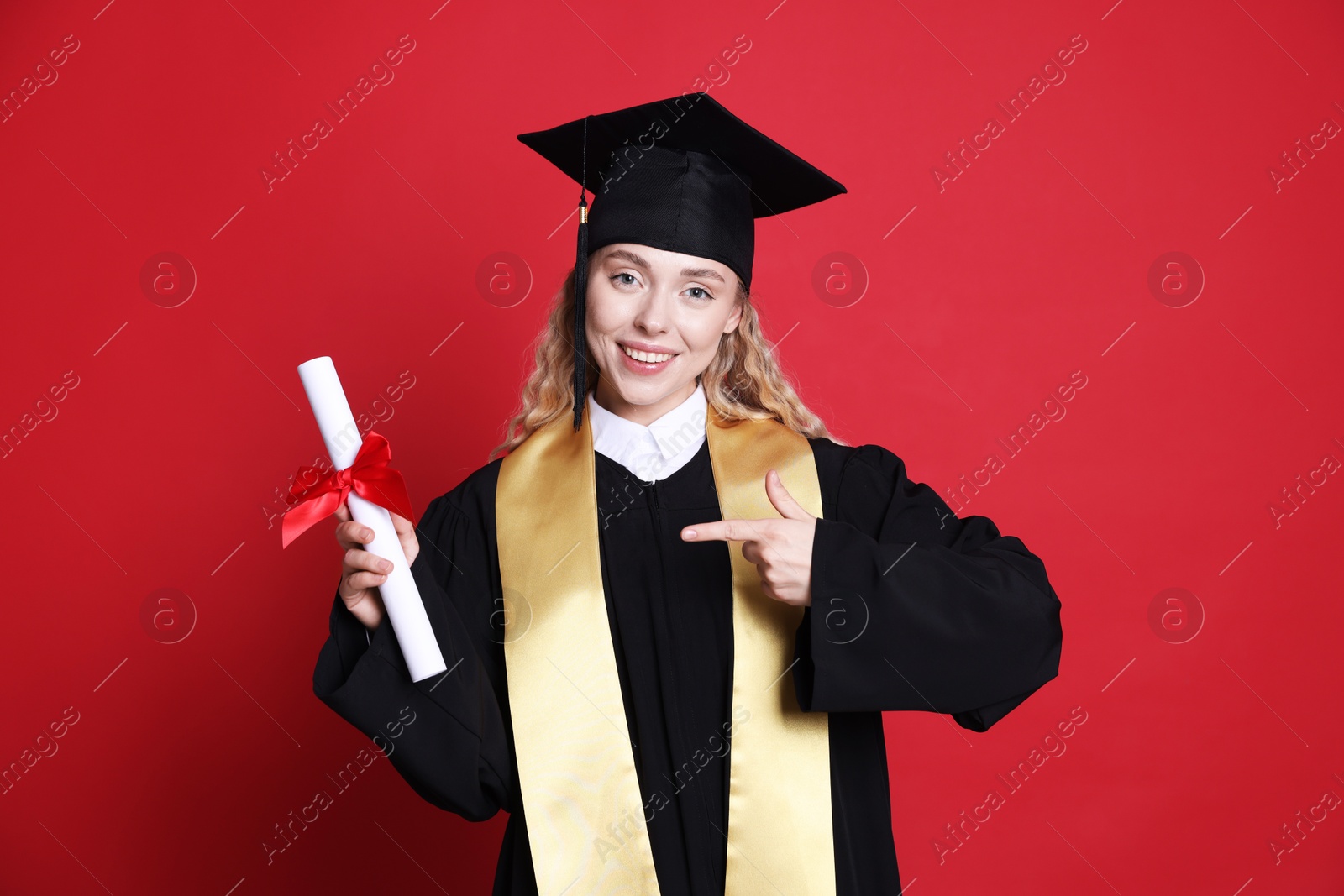 Happy student pointing at diploma after graduation on red background Photo of Happy student pointing at diploma after graduation on red background