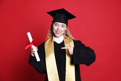 Photo of Happy student pointing at diploma after graduation on red background