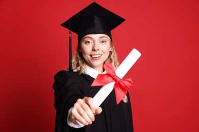 Photo of Happy student with diploma after graduation on red background, selective focus