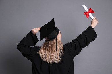 Photo of Student in mortarboard with diploma after graduation on grey background, back view