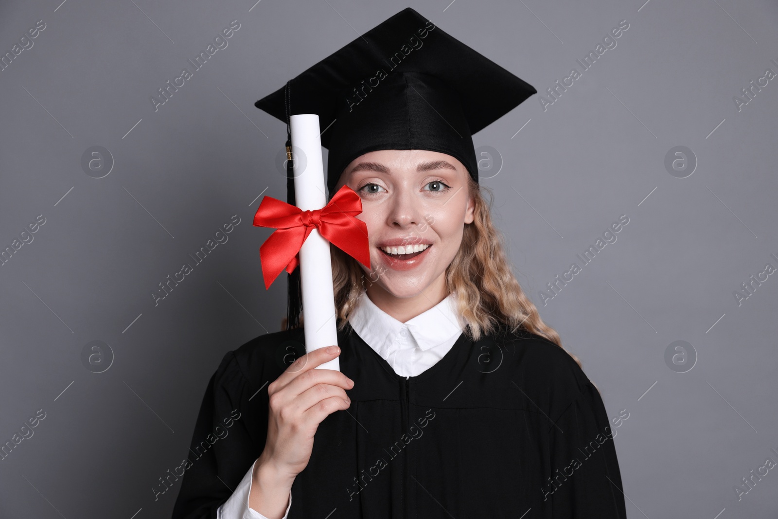 Happy student with diploma after graduation on grey background Photo of Happy student with diploma after graduation on grey background