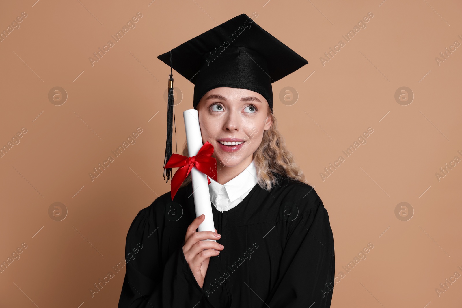 Happy student with diploma after graduation on beige background Photo of Happy student with diploma after graduation on beige background