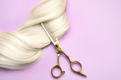 Image of Blonde hair strand and professional scissors on pink background, top view. Space for text