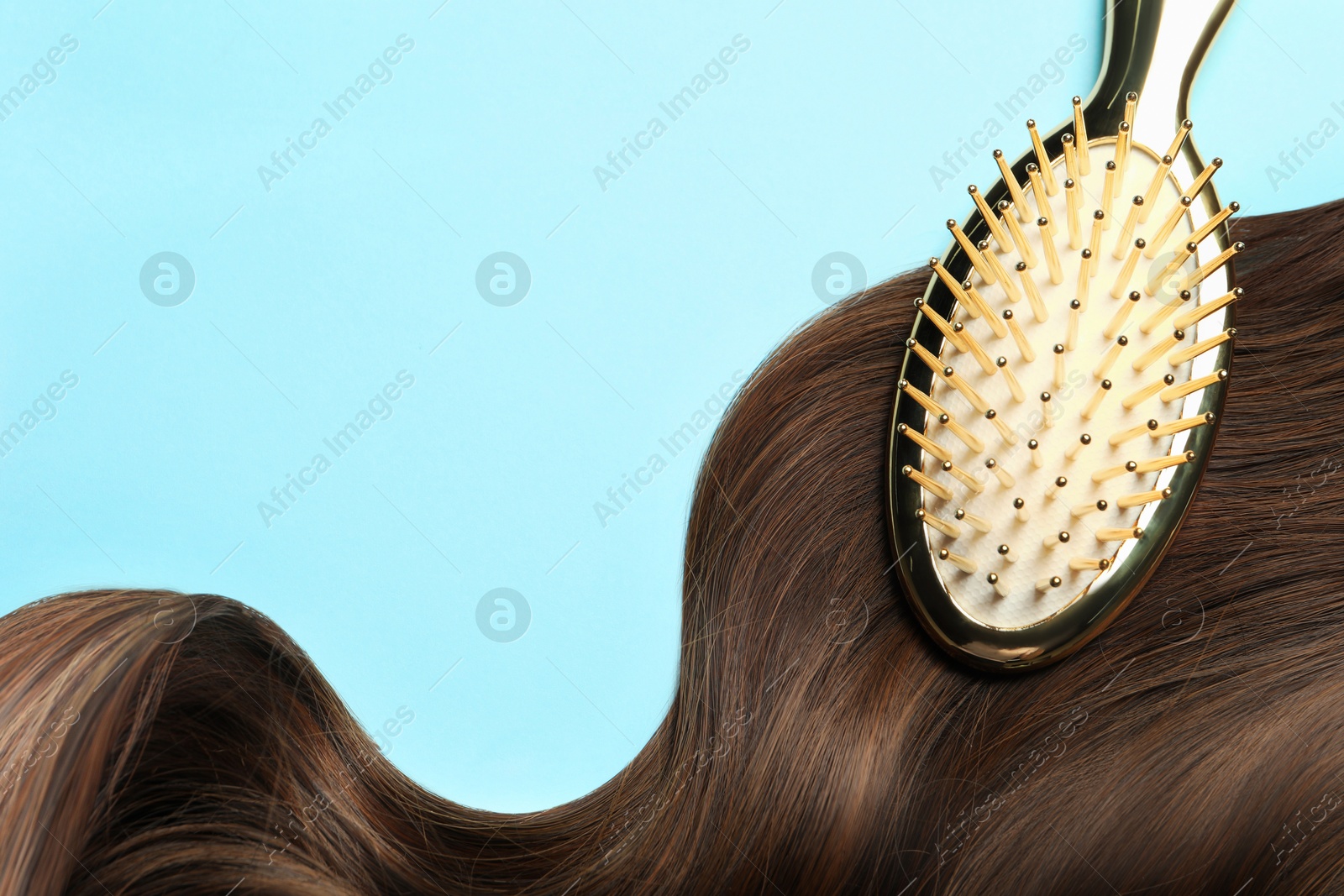 Brush with brown hair strand on light blue background, top view. Space for text Image of Brush with brown hair strand on light blue background, top view. Space for text