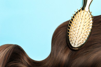 Image of Brush with brown hair strand on light blue background, top view. Space for text